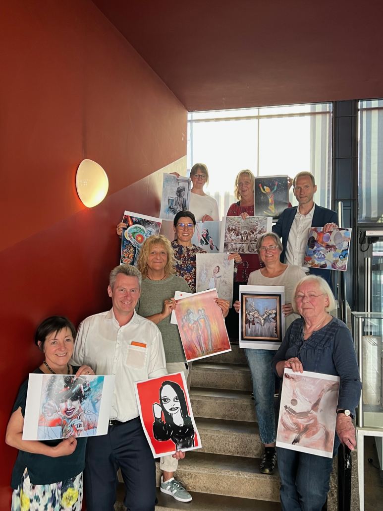 Frauen und Männer auf einer Treppe stehend. Jede/r hält ein Bild hoch.